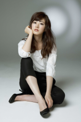 Ms. Rikomi is a Japanese & Asian mature beauty fashion model, she is wearing a white shirt and black pants, she sitting on the floor grasping her knees on the floor, her height is 171 cm and she is tall, her style is very good.