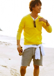 Mr. Takaatsu Sakurahaba is wearing a yellow long-sleeved shirt, beige shorts, he is standing on the sandy beach, he is a handsome Japanese & Asian actor, fashion male model.