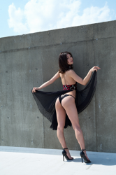 Ms. Yukina Fujihana is a Japanese & Asian gravure idol (swimsuit model), TV personality, and actress that has gradually become popular, she is wearing a black dress, she shows a beautiful back and buttocks, she is standing in front of a gray wall.
