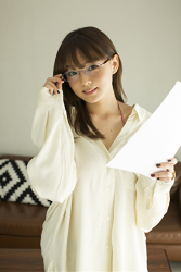 Ms. Aika's bust is 87 cm, she has big breasts and wears glasses, the Japanese & Asian cute big breasted gravure idol (swimwear model), Ms. Aika is wearing white casual clothes and holding a few sheets of paper, she is a sexually attractive woman, she is standing.