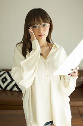 Ms. Aika Shinoba has big breasts and wears glasses, the Japanese & Asian cute big breasted gravure idol (swimwear model), Ms. Aika Shinoba is wearing white casual clothes and holding a few sheets of paper, she is a sexually attractive woman, she is standing.