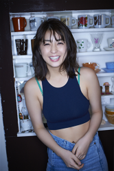 Ms. Yurine Yanagioka is wearing dark blue tank pop, Jeans, she is standing, and many cups are displayed behind her, she is a Japanese & Asian actress, swimsuit model (bikini model, swimsear model, gravure idol), TV personality, her bust is 84 cm, she has beautiful breasts.