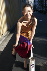 Ms. Aisui Saito is wearing a yellow dress, blue/red two-color skirt, she is in a city in Japan, she is a Japanese & Asian beautiful and sexy gravure idol (bikini model, swimsuit model, pin-up girl), actress, her bust is 85 cm, she has beautiful breasts, she is a sexually attractive woman.