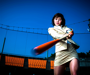 Ms. Amiri Inagawa is wearing a beige woman's suit and swinging a baseball bat, she is a beautiful and lively Japanese & Asian TV personality, swimsuit female model, baseball enthusiast, her bust is 86 cm, and she has beautiful breasts.