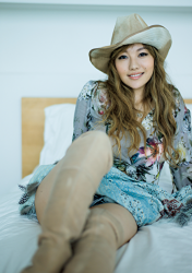 Ms. Hinana Tanigaki is wearing (with floral pattern) light blue blouse, she is wearing denim shorts, she is wearing a cowboy hat, she is sitting with her legs stretched out on the bed, she is a beautiful and sexy Japanese & Asian mature swimsuit model (swimwear model, bikini model), singer-songwriter, female Actor, yoga teacher, nutrition consultant, her bust is 88cm, she has big breasts, beautiful breasts.