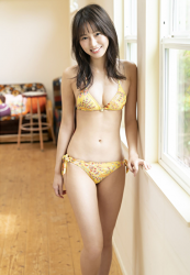 Ms. Neiro Shii wears a yellow bikini swimsuit, a young and very cute Japanese & Asian bikini model (gravure idol, swimsuit model, pin-up girl), TV personality, freelance announcer, with a smile on her face, she is standing by the window.