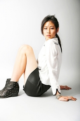 Ms. Mira Nagase is wearing a white shirt, black miniskirt, black shoes, she is sitting on the white floor, she is a Japanese & Asian tall fashion model, runway model (catwalk model), her height is 179 cm, she is a tall, slender model.