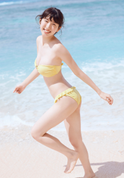The Japanese & Asian gravure idol (pin-up girl / swimsuit model), actress, and singer in a yellow bikini is on the beach, she is standing and smiling, her name is Mikoto Hizaka.