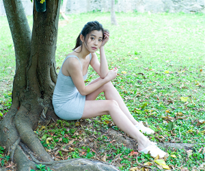 Ms. Ayami Asashige is wearing a gray dress, she is sitting by the tree, she is a tall Japanese & Asian beautiful and elegant fashion model, gravure idol (bikini model, swimsuit model, pin-up model), TV entertainer, actress.