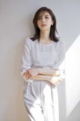 Ms. Akie Shibukawa is a beautiful Japanese & Asian fashion model, she is dressed in white and stands against a wall.