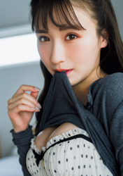 Ms. Emina Iori is a Japanese and Asian gravure idol (swimwear model, bikini model, pin-up girl), TV personality and singer, she is wearing a gray long-sleeved shirt and a white bra, standing in a room, and this photo has her face highlighted.