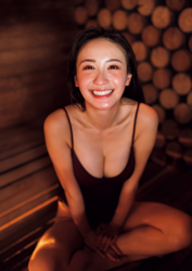 Ms. Emina Iori is a Japanese and Asian gravure idol (swimwear model, bikini model, pin-up girl), TV personality and singer, she's in a sauna room, she's wearing a purple bathing suit, she's sitting, and she's smiling.