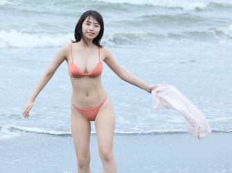 Ms. Kiira Kikuoki is a Japanese & Asian gravure idol (swimwear model, bikini model, pin-up model) and actress, she is at the beach, stripped of her white shirt and wearing an orange bikini, she is standing on the beach.