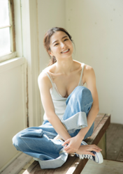 Ms. Mariho Kokei is a Japanese & Asian fashion model, swimsuit model (gravure idol), actress, and former idol, she wears a light gray shirt and jeans and sits on a bench inside the house.