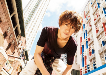 Mr. Ayato Akaibashi is sitting on a street corner in Hong Kong wearing a red shirt and white pants, he is also an actor and voice actor.