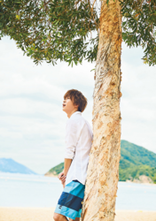 Mr. Ayato Akaibashi is wearing a white shirt and light blue shorts and is standing under a tree, he is also an actor and voice actor.