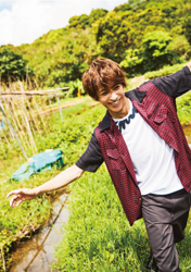 Mr. Ayato Akaibashi is standing in the grass, wearing dark summer clothes and also a white shirt, he is also an actor and voice actor.