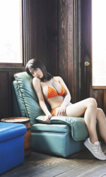 Ms. Kiira Kikuoki is a Japanese & Asian gravure idol (swimwear model, bikini model, pin-up model) and actress, she is wearing an orange bikini and sitting on a green sofa.