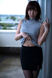 Ms. Kirina Hinaga is wearing a gray shirt and a black skirt and is standing on the balcony, she is a Japanese & Asian sweet and cute big breasts gravure idol (pin-up model, bikini model, swimsuit model), her bust is 90 cm, she has charming big breasts, she is a woman with sexual charm.