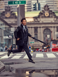 Mr. Takaatsu Sakurahaba is wearing dark clothes, holding an umbrella in his hand and jumping a little at the crosswalk, he is a handsome Japanese & Asian actor, fashion male model.