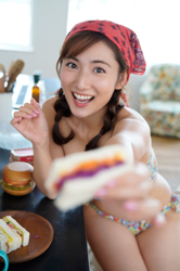 Ms. Yaaya Igeta is wearing a colorful bikini and a red cloth around her head, sitting by the kitchen, holding a sandwich, she is a Japanese & Asian gravure idol (bikini model, swimsuit model, pin-up girl), actress, TV personality, her bust is 92 cm, she has attractive big breasts, she is a sexually attractive woman.