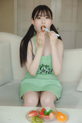 Ms. Asumi Saigosawa is wearing a yellow-green apron, sitting on a white sofa and eating fruit, she is a very cute and young actress who is also active as a bikini model (swimsuit model / gravure idol / pin up girl).