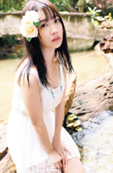 Ms. Kisara Amakura is a Japanese active idol, a very cute bikini model (gravure idol), an actress, and a TV personality, she is by the river, sitting on a fallen tree, and she is wearing a white dress.
